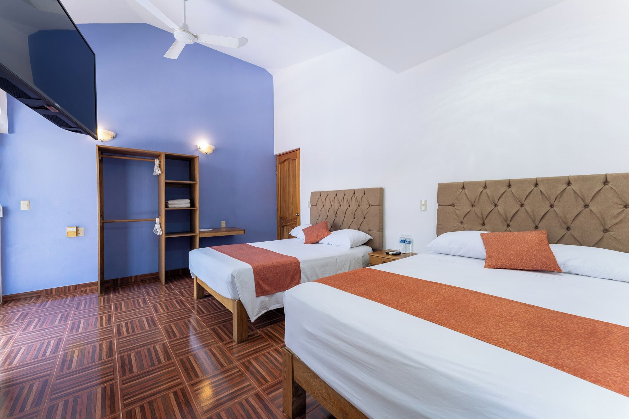 Ein Hotelzimmer mit zwei Betten, einem Schrank, einem Deckenventilator und Holzboden.
