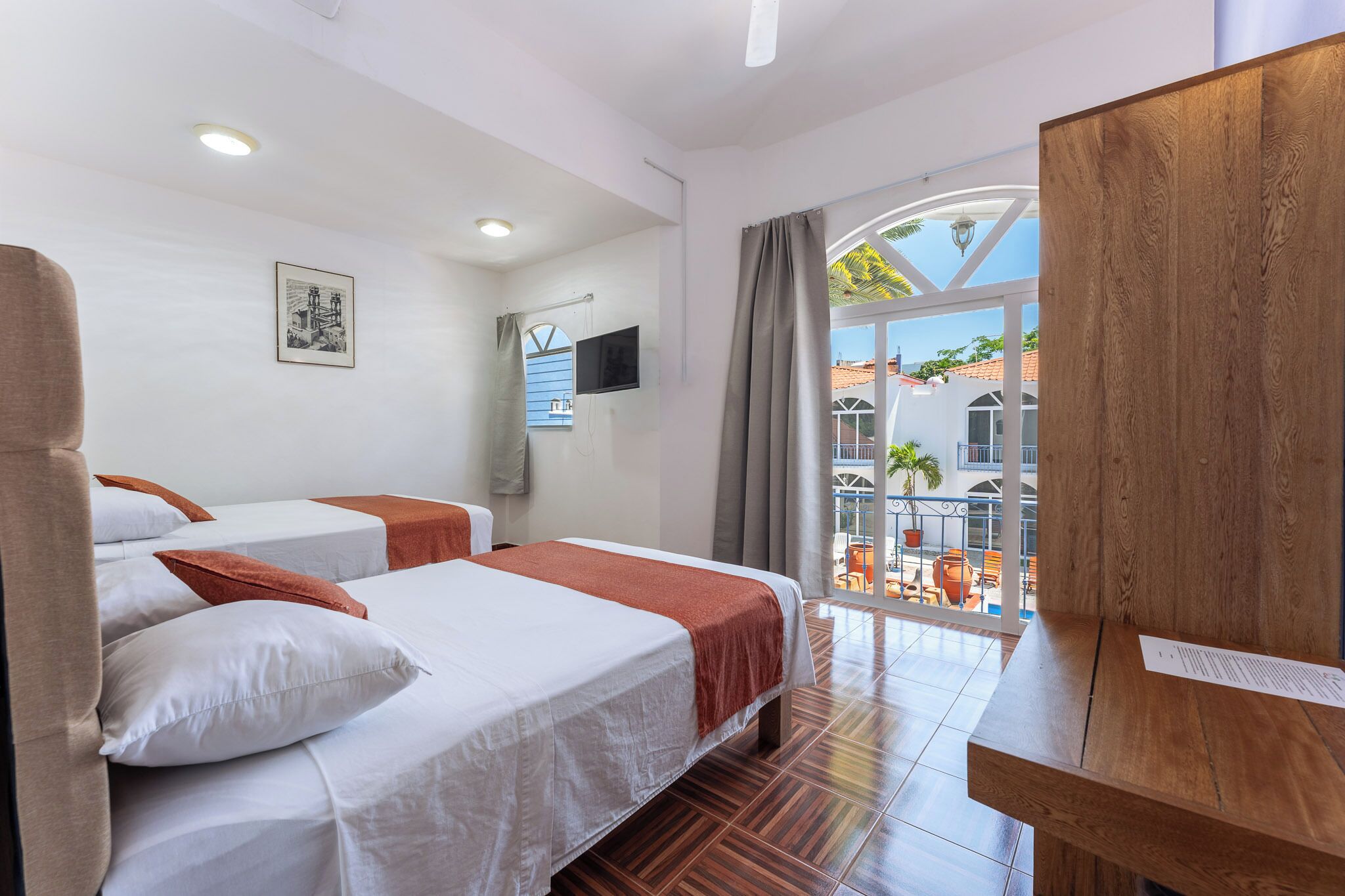 A hotel room with two beds, a TV, a wooden desk, and a balcony with outdoor furniture.