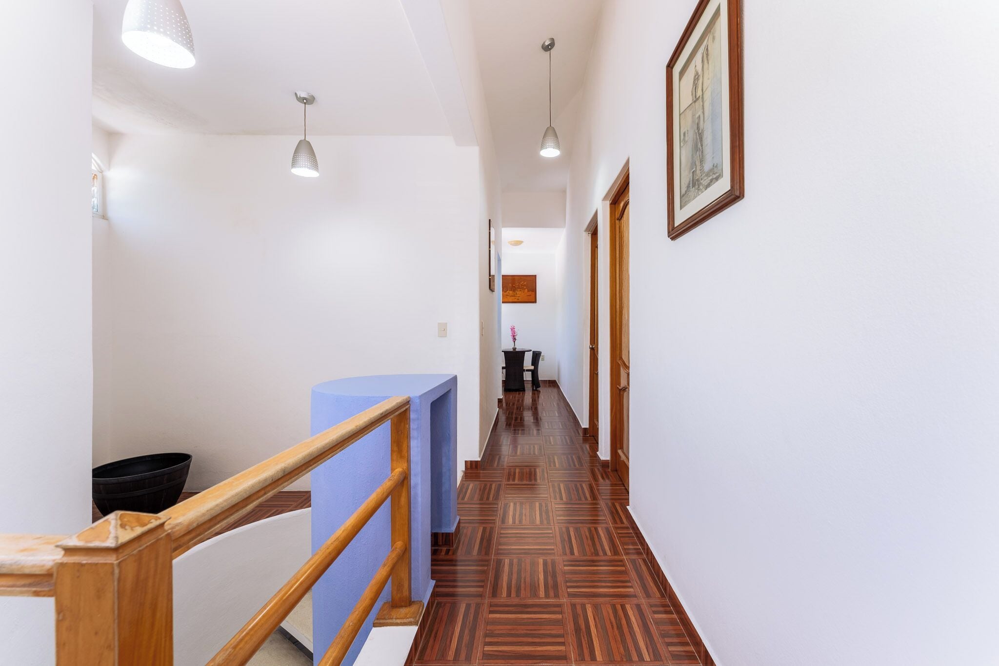 A hallway with wooden railings, patterned flooring, and pendant lighting.