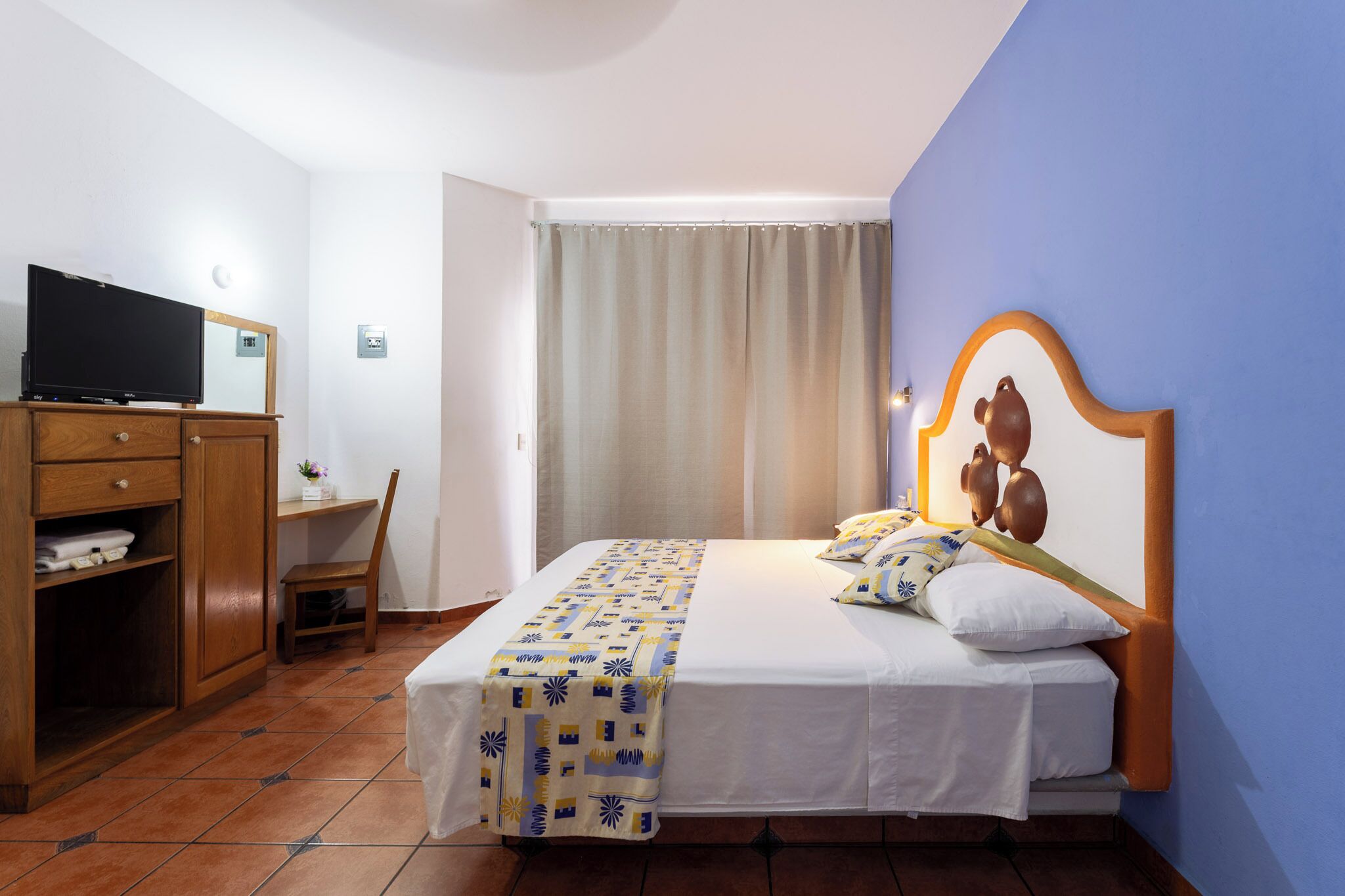 A hotel room with a bed, a television, a desk, and a chair.