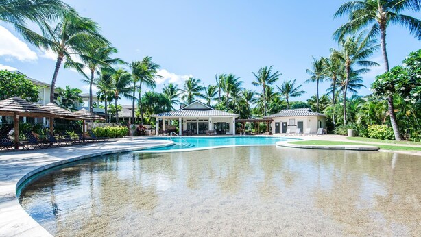 Ein Poolbereich eines Resorts mit klarem, blauem Wasser, Liegestühlen und Palmen.