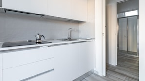 Una cocina moderna con armarios blancos, un lavamanos de acero inoxidable y un hervidor.