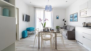 Una cocina moderna con armarios blancos, un comedor con mesa y sillas, un sofá y un televisor montado en la pared.