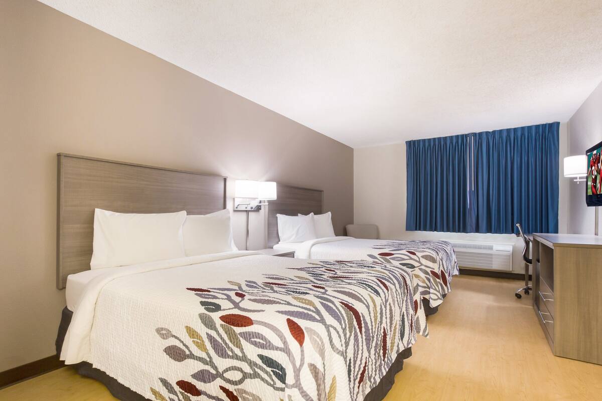 Quarto de hotel com uma cama grande, uma mesa de trabalho e uma janela com cortinas azuis.