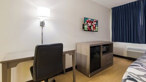 A hotel room with a desk, a chair, a television mounted on the wall, a microwave, and a bed with a patterned bedspread. - Red Roof Inn Lawrenceburg (Lawrenceburg)