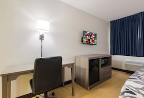 Habitación de hotel con escritorio, silla, televisión montada en la pared, microondas y cama con colcha estampada.
