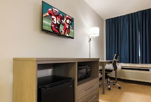Quarto de hotel com televisão de tela plana na parede, uma mesa com cadeira, micro-ondas e aquecedor.