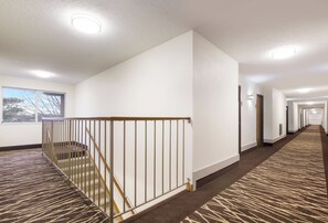 A hotel corridor with a carpeted staircase, white walls, and a view of the outside through a window. - Red Roof Inn Lawrenceburg (Lawrenceburg)