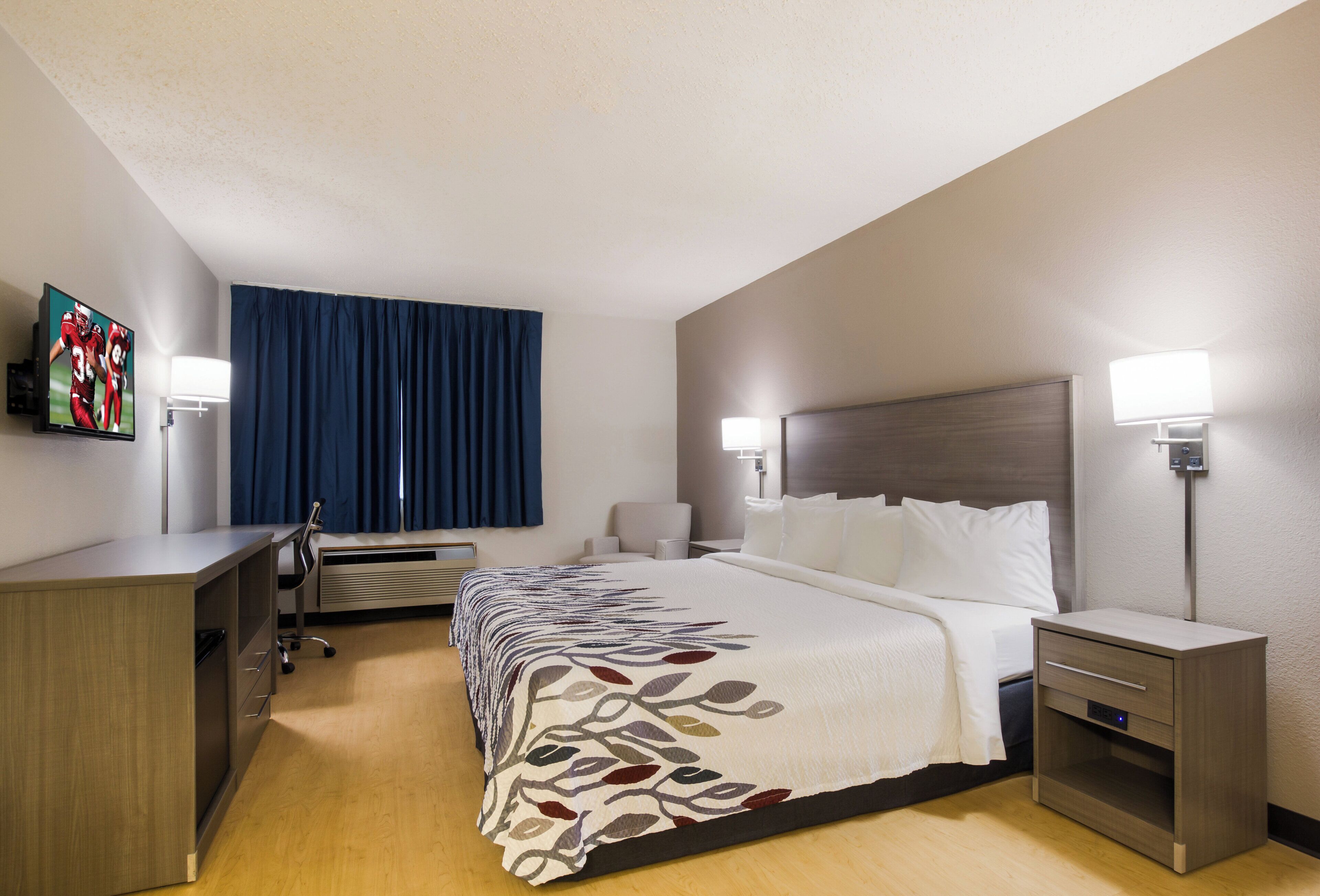 Habitación de hotel con cama, mesitas de noche, escritorio, silla, televisor y ventana con cortinas.