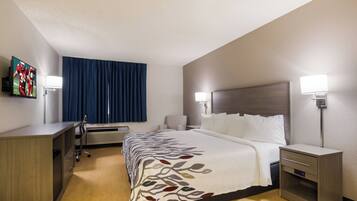 Habitación de hotel con cama, mesitas de noche, escritorio, silla, televisor y ventana con cortinas.