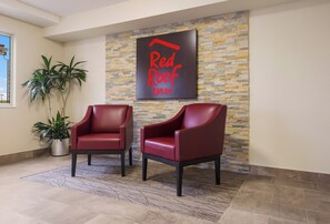 A lobby area with two red leather chairs, a potted plant, and a wall with a sign reading 'Red Roof Inn'. - Red Roof Inn Lawrenceburg (Lawrenceburg)