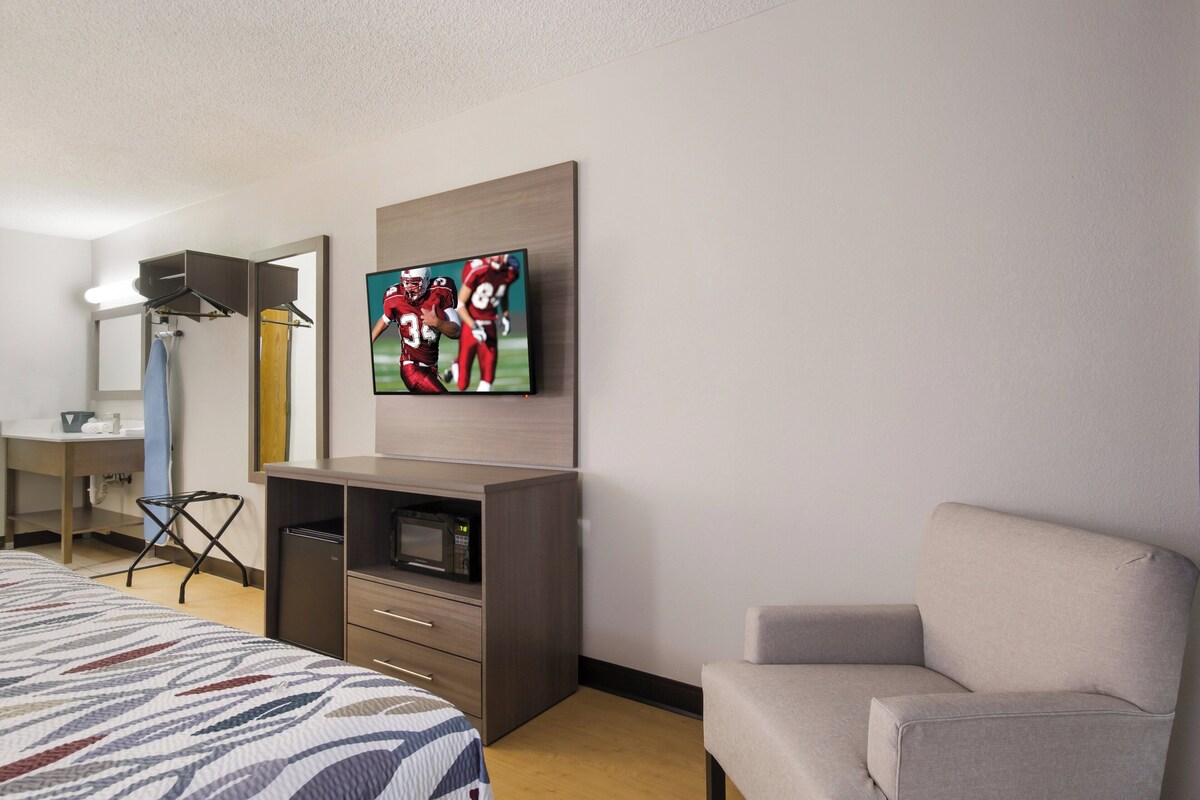 Een hotelkamer met een bed, een aan de muur bevestigde televisie, een bureau met een magnetron en een stoel.