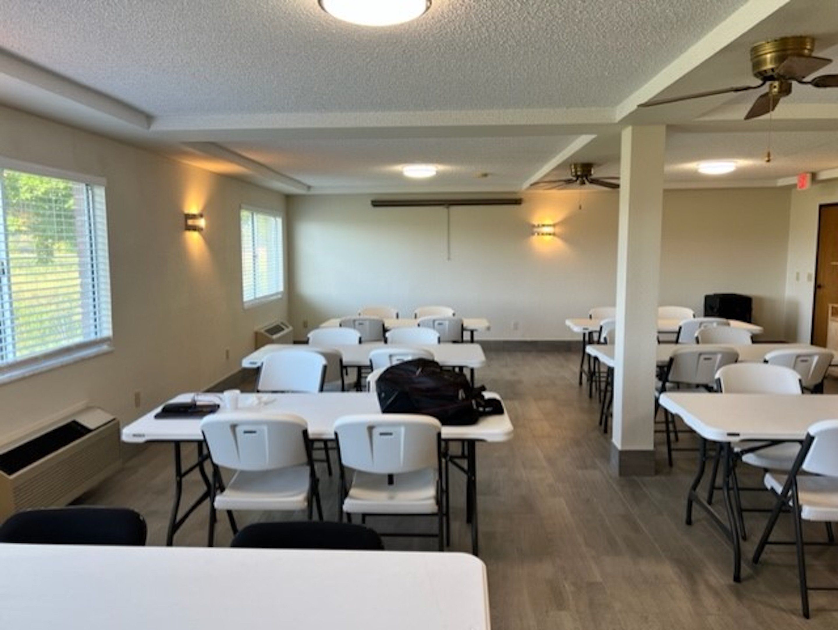 A conference room with white tables and chairs, a ceiling fan, and a window with blinds.