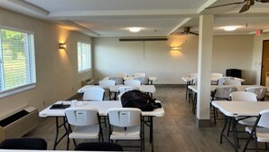 A conference room with white tables and chairs, a ceiling fan, and a window with blinds.