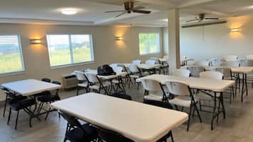 A conference room with tables and chairs, ceiling fans, and windows with blinds.
