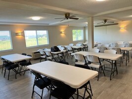 Un salón de conferencias con mesas, sillas, ventiladores de techo y ventanas con persianas.
