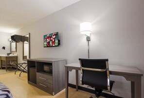 Habitación de hotel con cama, escritorio, silla, televisor, espejo y lámpara.