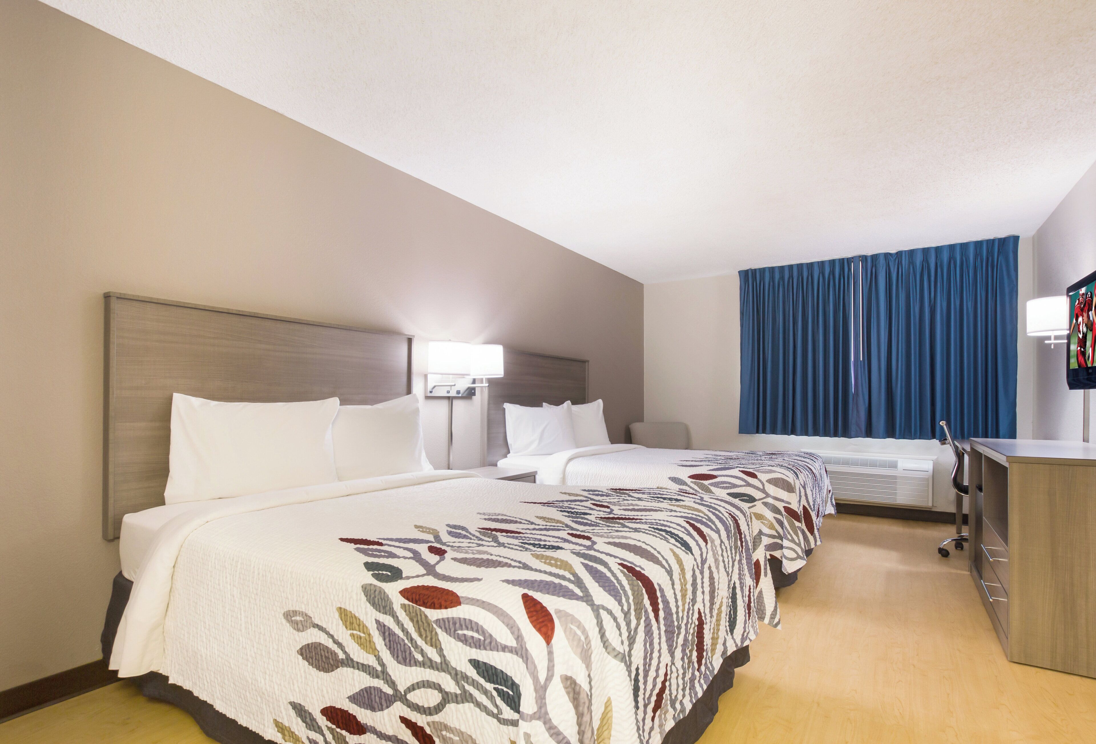 A hotel room with two beds, a desk, and a television.