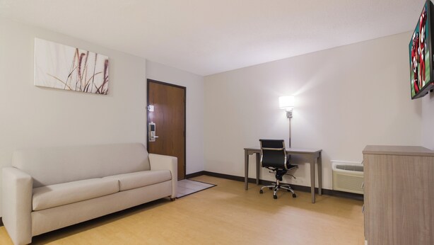 A room with a sofa, a desk with a chair, a standing lamp, and a radiator. - Red Roof Inn Lawrenceburg (Lawrenceburg)