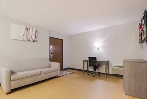A room with a sofa, a desk with a chair, a standing lamp, and a radiator. - Red Roof Inn Lawrenceburg (Lawrenceburg)
