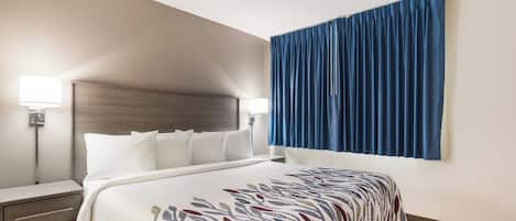 Une chambre d’hôtel avec un lit, des lampes de chevet, un ventilateur de plafond et une grande fenêtre avec des rideaux bleus.