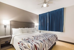 Habitación de hotel con cama, lámparas de noche, ventilador de techo y un ventanal con cortinas azules.