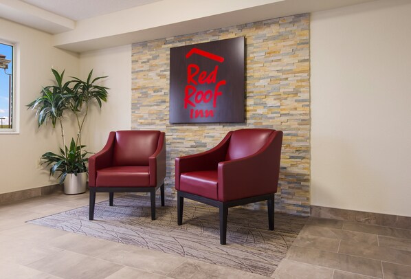 A Red Roof Inn lobby with two red leather chairs, a stone wall, and a potted plant. - Red Roof Inn Lawrenceburg (Lawrenceburg)