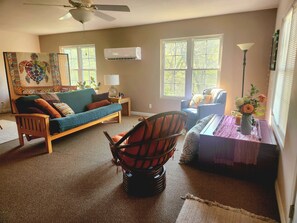 Un salon avec un canapé, des fauteuils, une lampe, un vase de fleurs et un ventilateur de plafond.