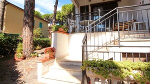 Un edificio de dos pisos con una escalera que conduce a un balcón. Hay plantas en macetas en la planta baja y una barandilla de metal en el piso superior.