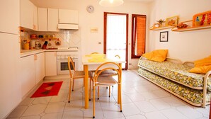 Un espacio habitable compacto con kitchenette, zona de comedor con mesa y sillas, sofá con cojines y cama.