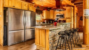 A modern kitchen with wooden cabinets, a stainless steel refrigerator, a granite countertop, and bar stools.