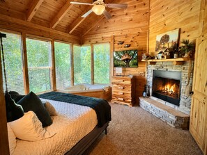 Ein Holzhütten-Interieur mit Bett, Kamin und großen Fenstern.