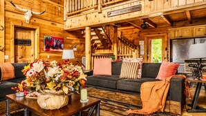 A log cabin interior with a wooden staircase, a dining area, and a living room with a sofa and a coffee table.