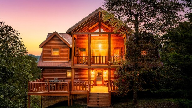 A two-story log cabin with a porch and a staircase leading to the entrance.