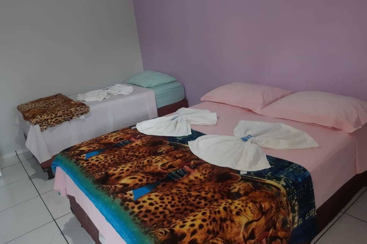 Ein Hotelzimmer mit zwei Betten, eines mit einer leopardenmuster Tagesdecke und das andere mit einer schlichten weißen. Auf den Betten liegen Handtücher und auf dem Nachttisch eine Decke mit Leopardenmuster.