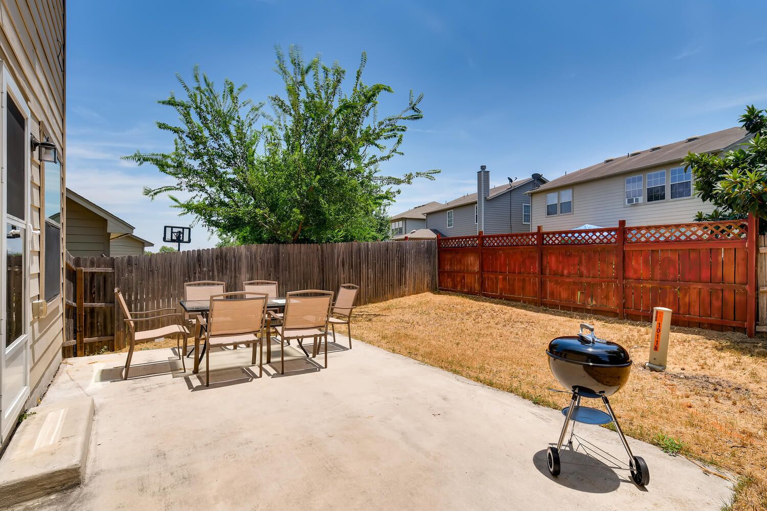 A backyard with a concrete patio, a barbecue grill, a wooden fence, and a tree.