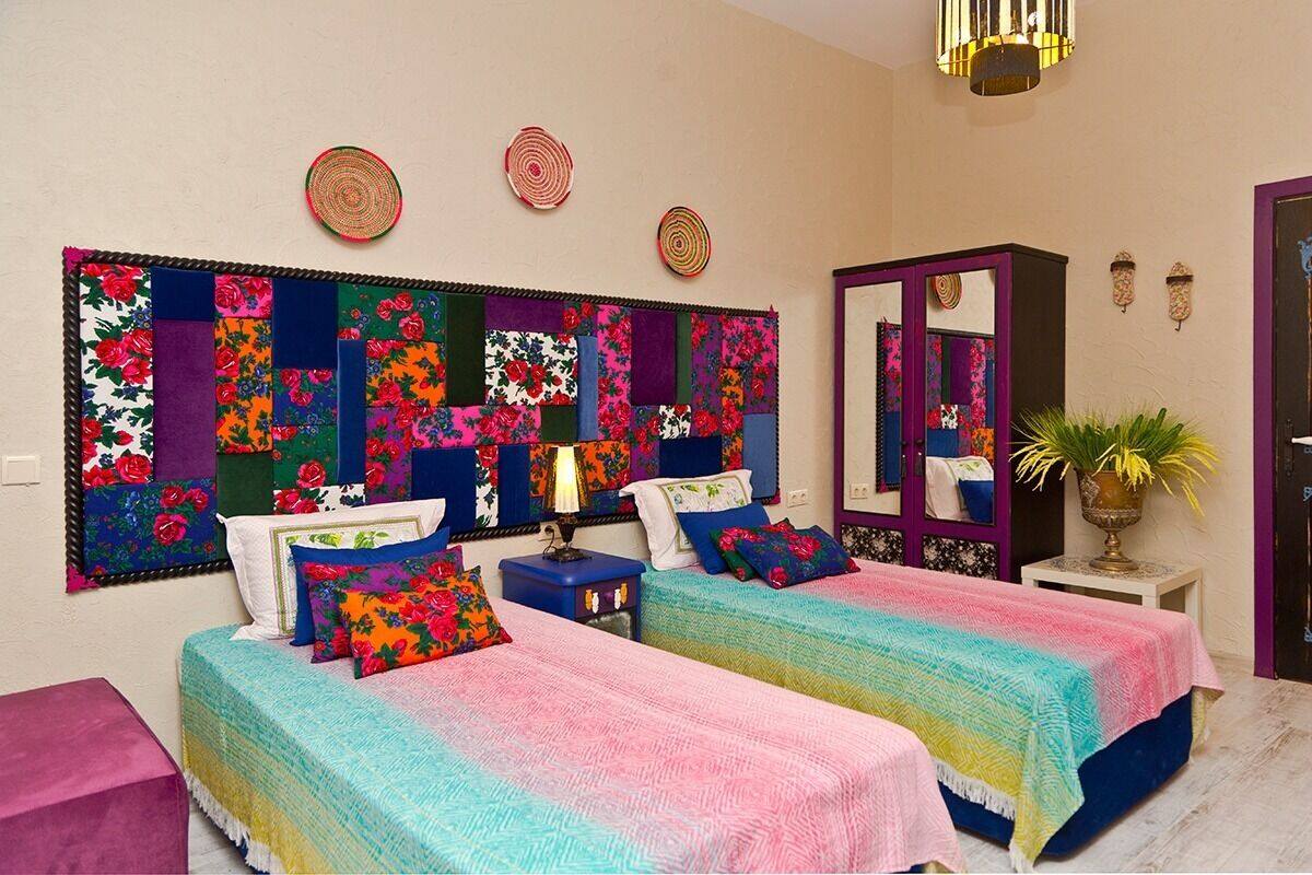 A bedroom with two beds, colorful bedding, a large decorative headboard, a mirror, and a small table with a plant.