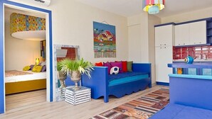 A compact living space with a bed, a blue sofa, a small kitchen area, and a colorful artwork on the wall. - Palmiye Tepesi (Bodrum)