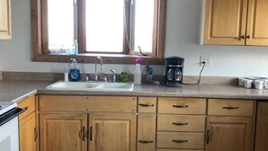A kitchen with wooden cabinets, a double sink, a window, and a coffee maker.
