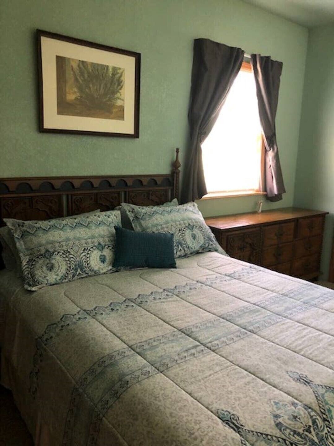 A bedroom with a bed, a dresser, a framed picture on the wall, and a window with curtains.