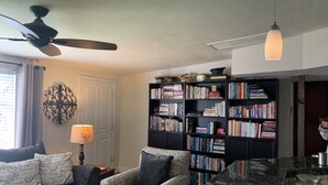 Een woonkamer met een bank, fauteuil en een grote boekenkast vol boeken.