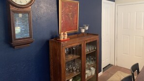 Een kamer met een houten klok, een kast met glazen deuren en een ingelijst schilderij aan de muur.