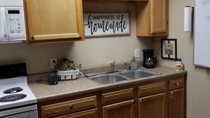 Una cocina con armarios de madera, microondas, fregadero y encimera con cafetera.