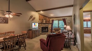 Una sala de estar acogedora con chimenea de piedra, comedor con mobiliario de madera y un amplio ventanal con cortinas.