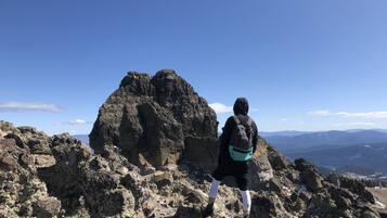 Uma pessoa em terreno rochoso com uma mochila, observando uma paisagem montanhosa.