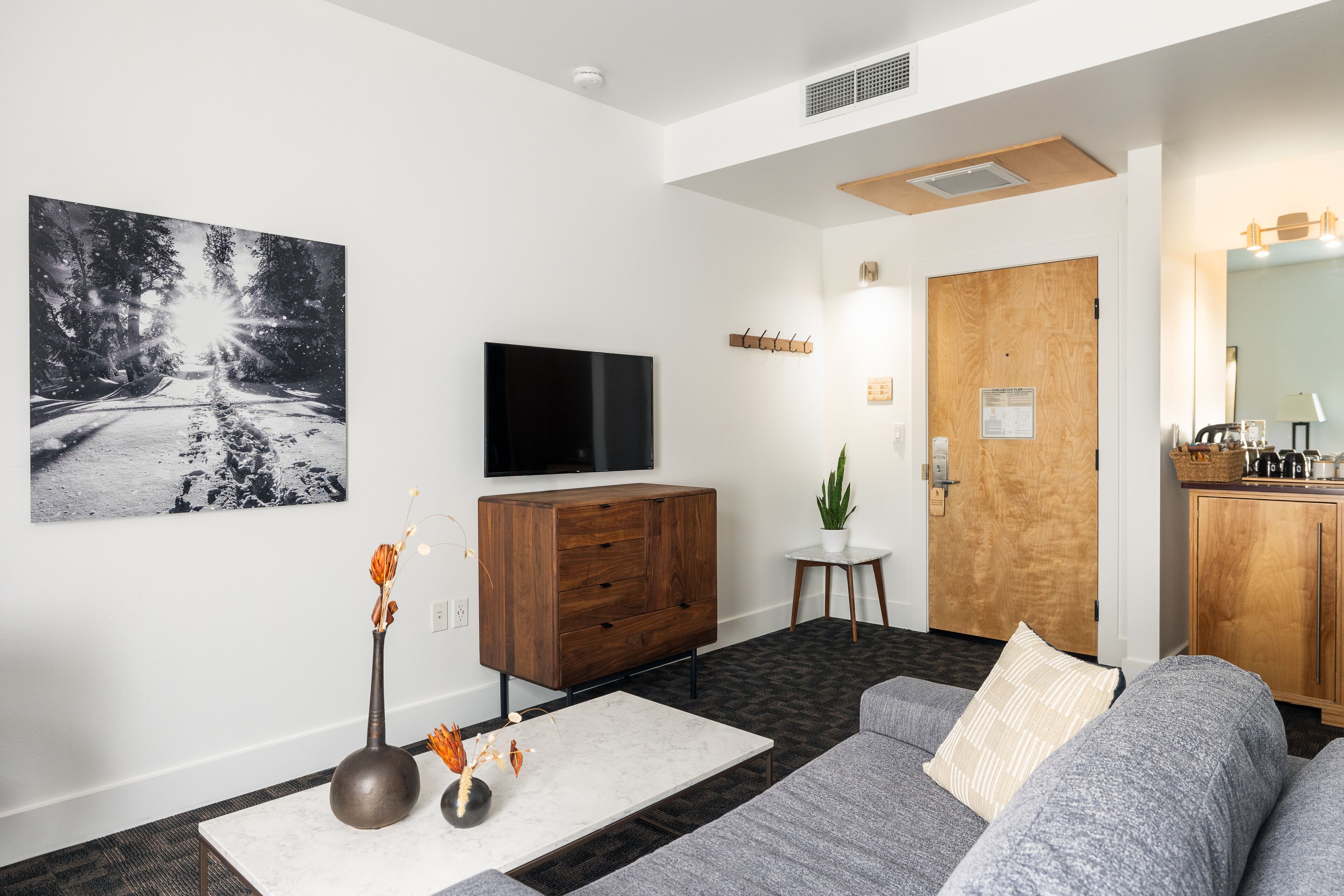A modern living room with a flat-screen TV, a wooden cabinet, a gray sofa, a white coffee table, and a black and white photograph on the wall.