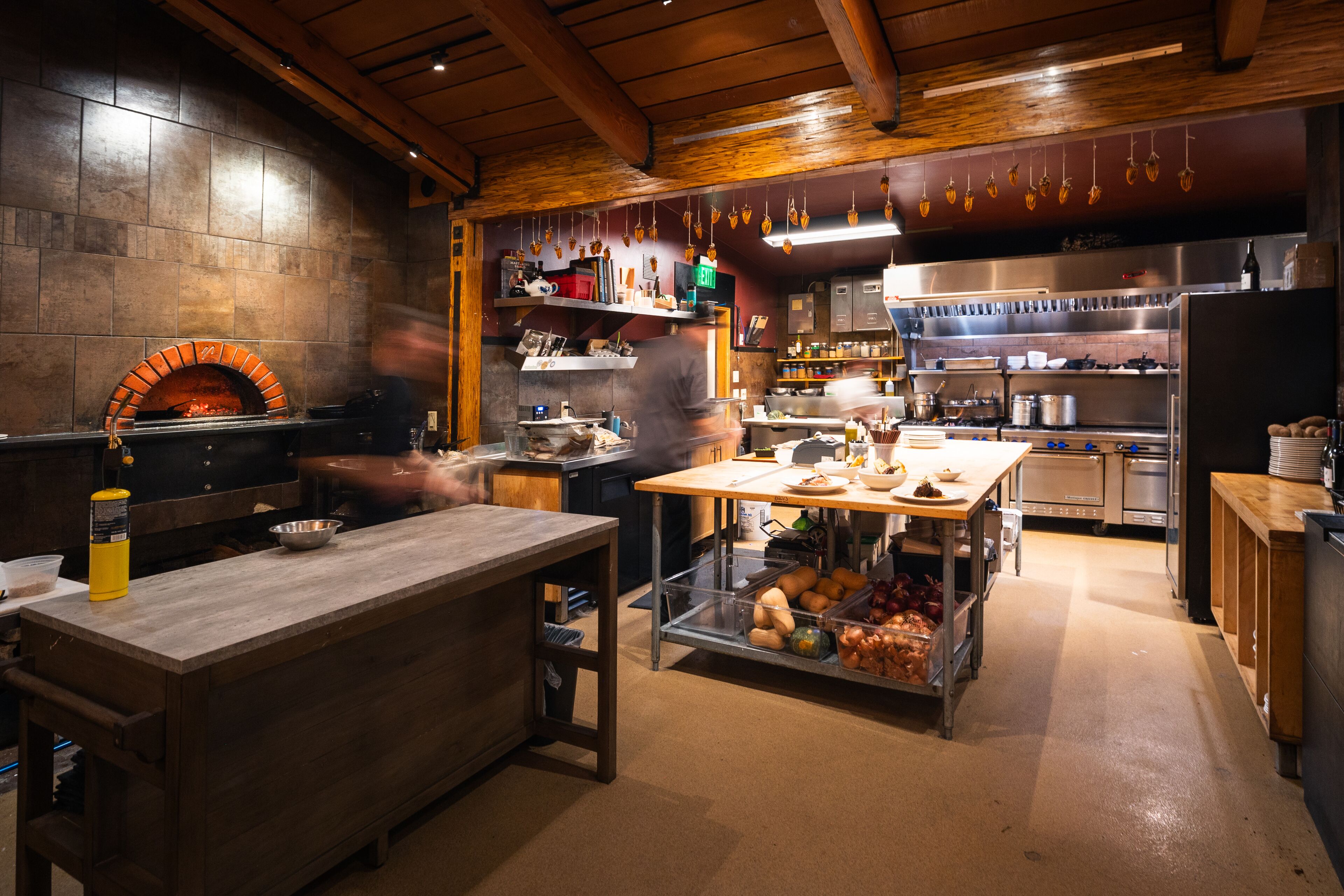 A kitchen with a wood-fired oven, stainless steel appliances, and a central island with a sink and counter space.