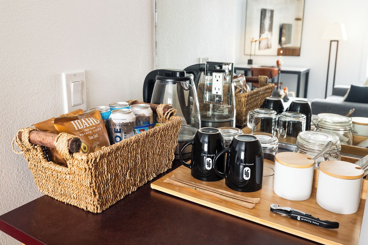 Une table en bois dressée pour le petit-déjeuner, avec un panier de collations, des tasses à café et des ustensiles de cuisine.