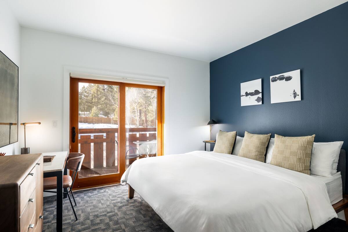 Un dormitorio con cama, escritorio, silla y vistas al exterior por una puerta corrediza.