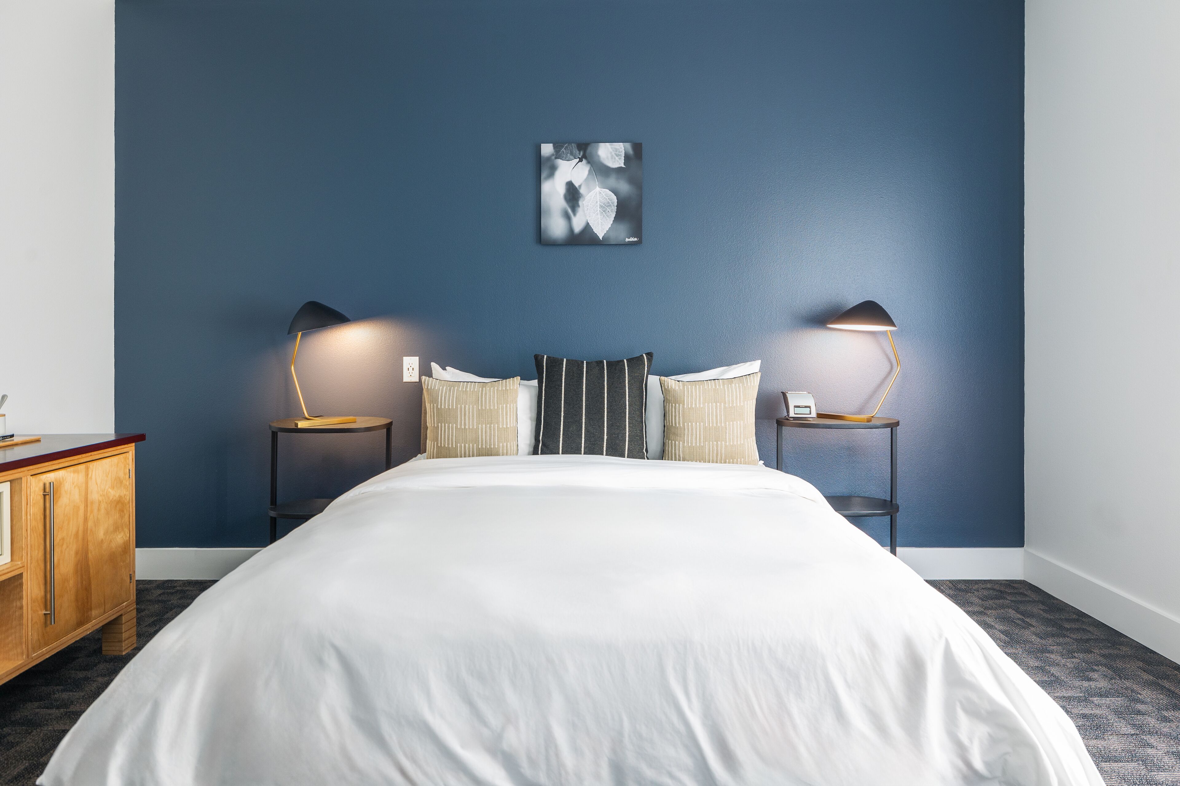 A neatly made bed with white linens, two bedside tables with lamps, and a framed artwork on the wall.
